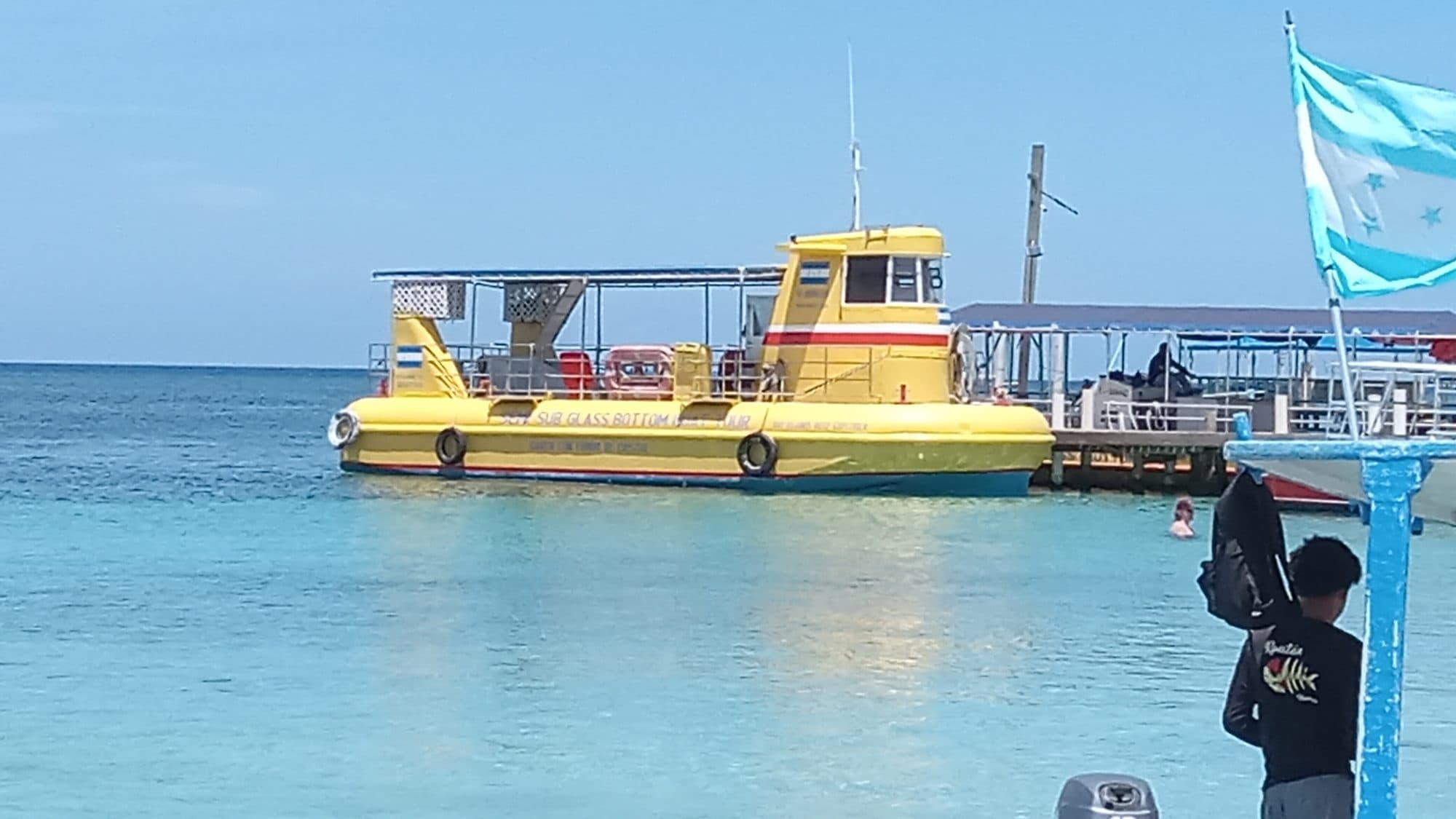 A yellow glass-bottom tour boat tied up at the dock in flat turquoise water