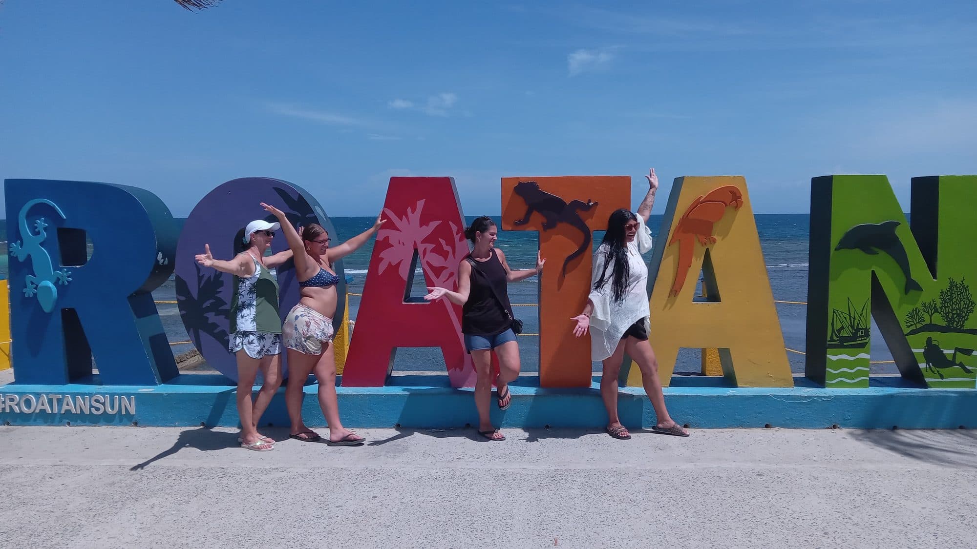 Cuatro visitantes posando juntas con los brazos abiertos entre las letras gigantes de ROATÁN