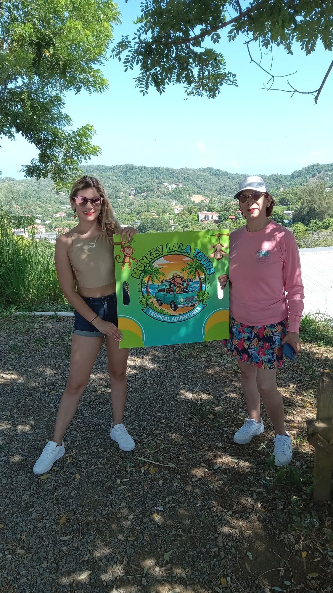 Dos guías de Monkey Lala sosteniendo el cartel pintado de la empresa en el punto de encuentro, con la ladera detrás