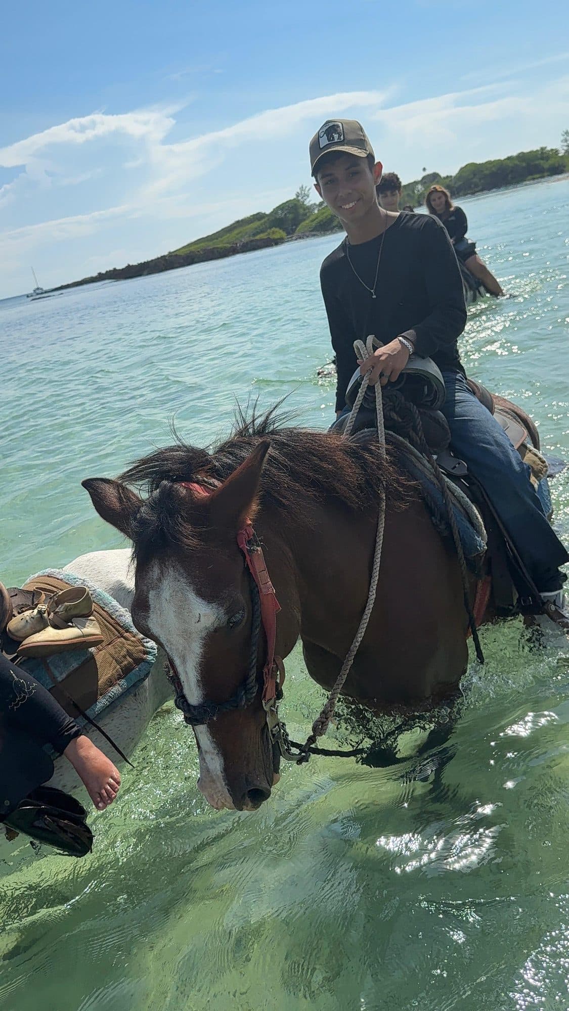 Un jinete sonriendo a caballo en la orilla, con las riendas en la mano y un islote a lo lejos