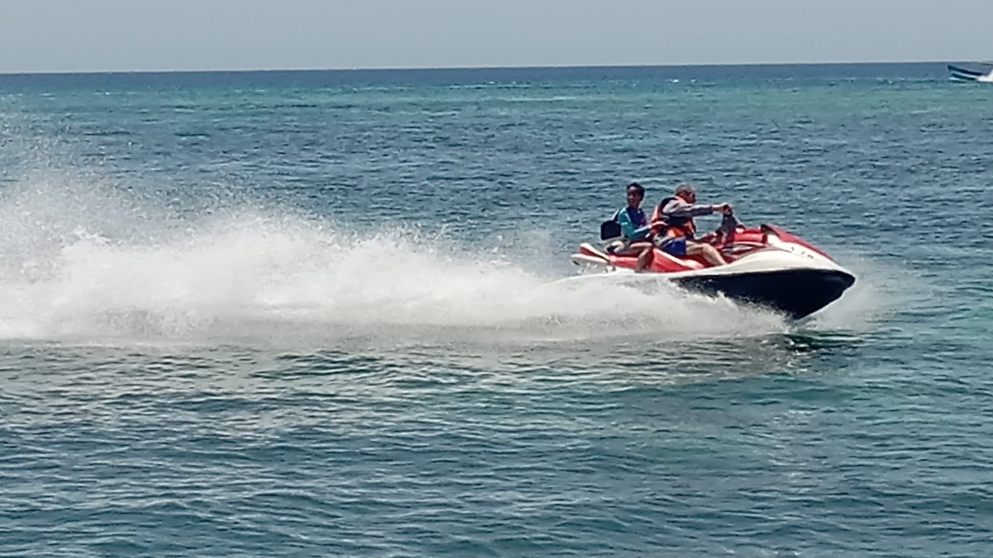 Dos visitantes conduciendo motos de agua a toda velocidad por la bahía, levantando una pared larga de espuma