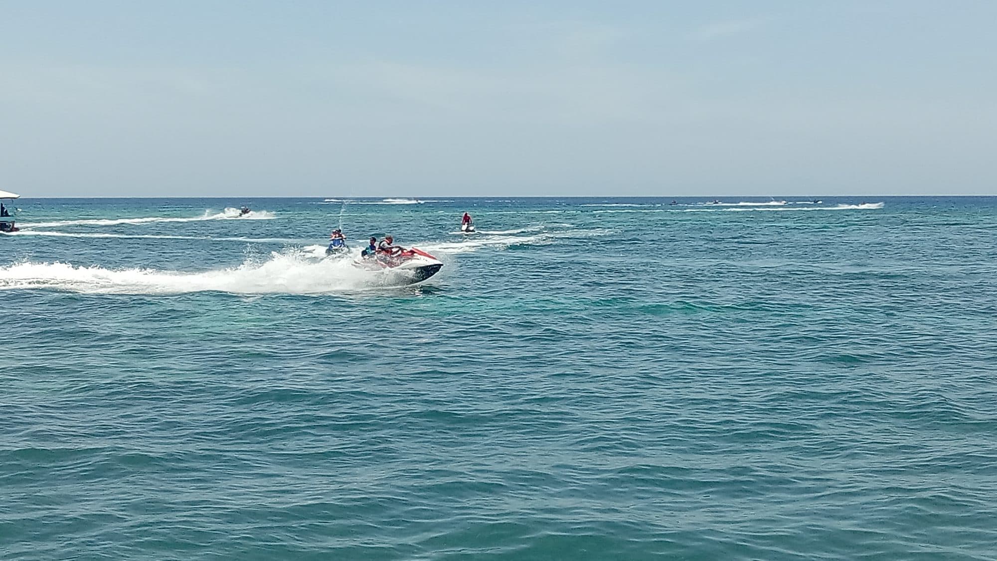 Motos de agua cruzando la bahía abierta con la línea del arrecife rompiendo en el horizonte