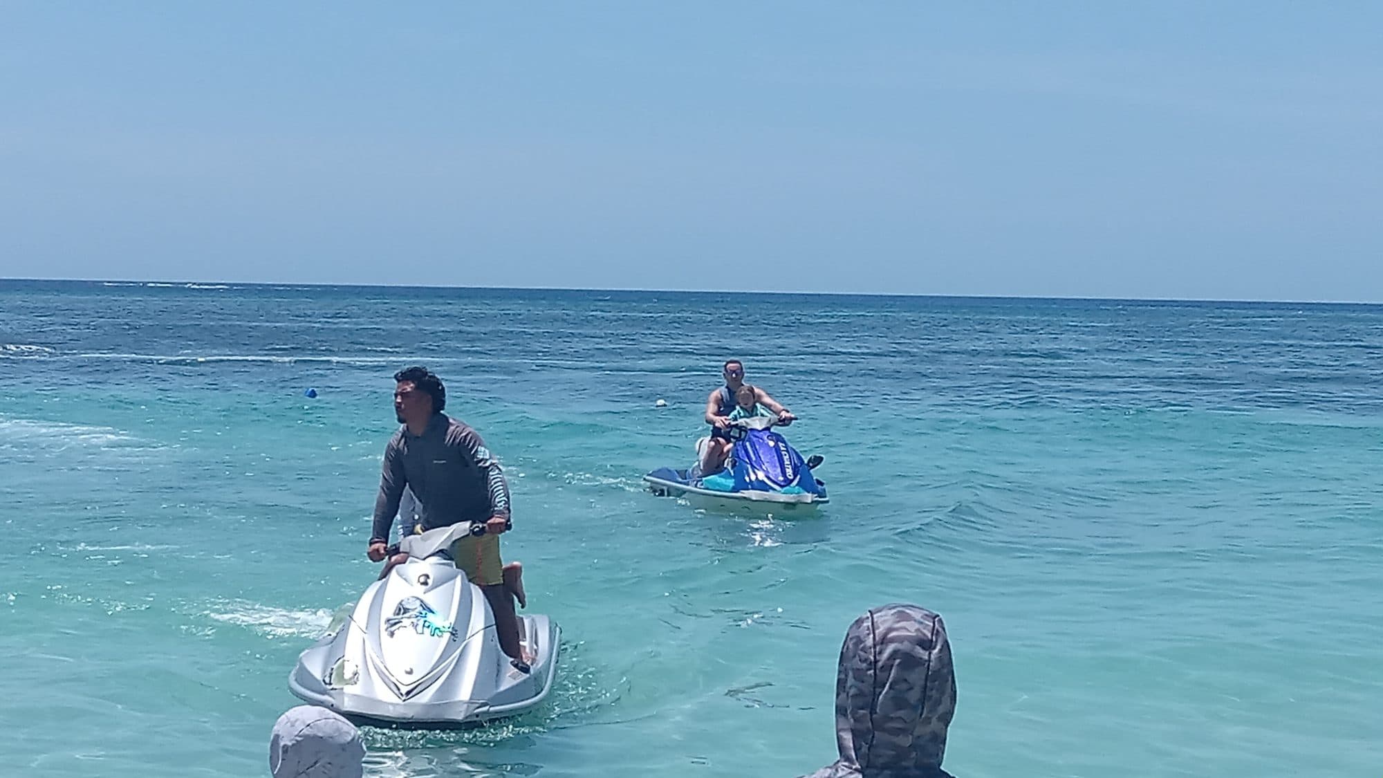 Dos motos de agua al ralentí en aguas bajas turquesa con sus conductores de pie sobre los estribos