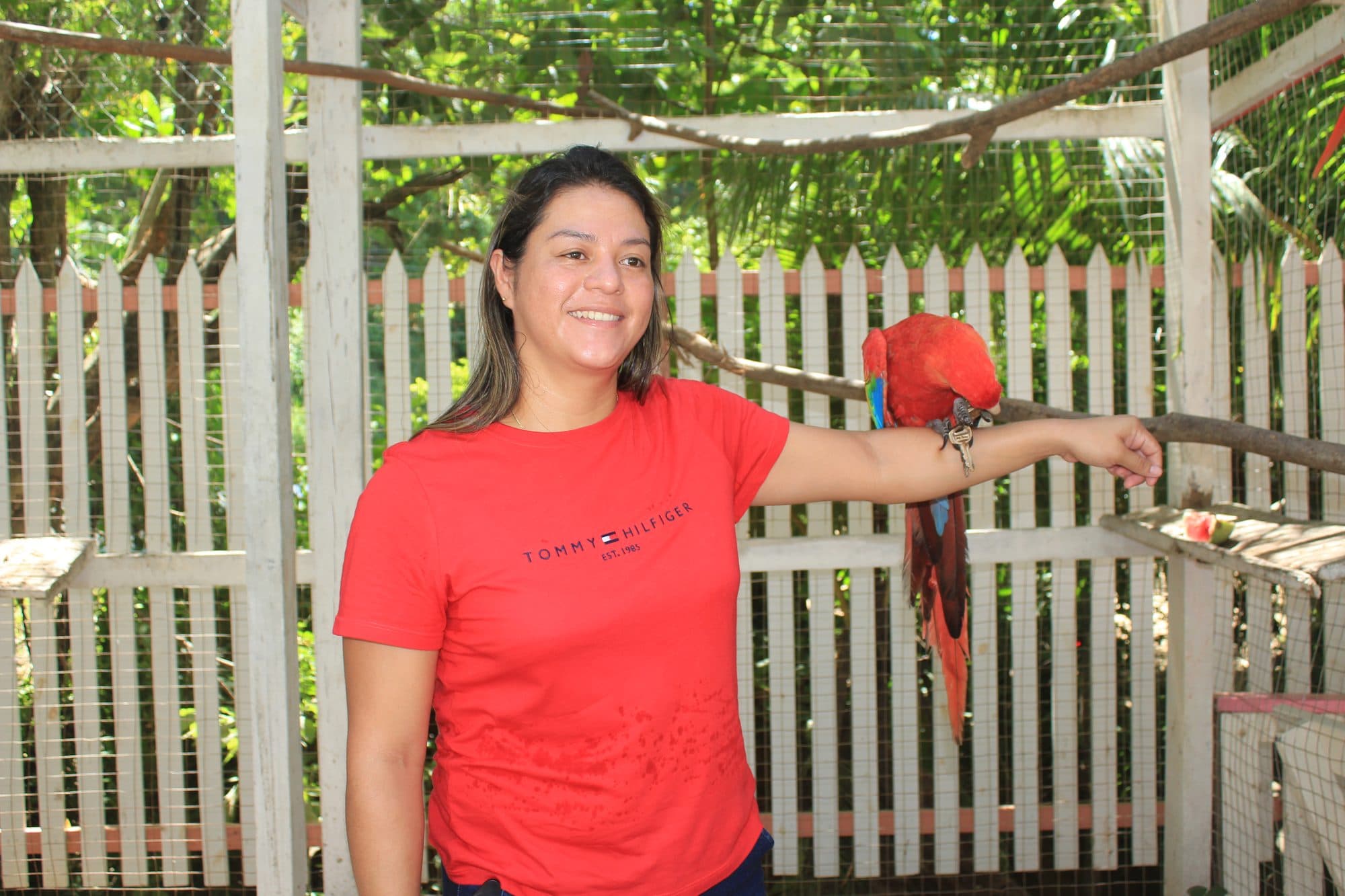Una visitante de camiseta roja con una guacamaya roja en equilibrio sobre su brazo extendido
