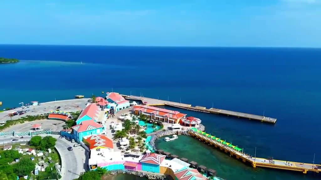 Los tejados de colores del pueblo del puerto y su muelle vistos desde el aire, con el arrecife al fondo