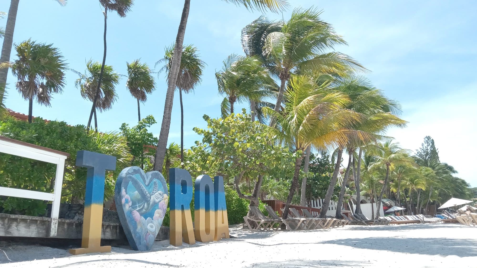 El corazón pintado y las primeras letras del rótulo de ROATÁN sobre la arena entre cocoteros altos