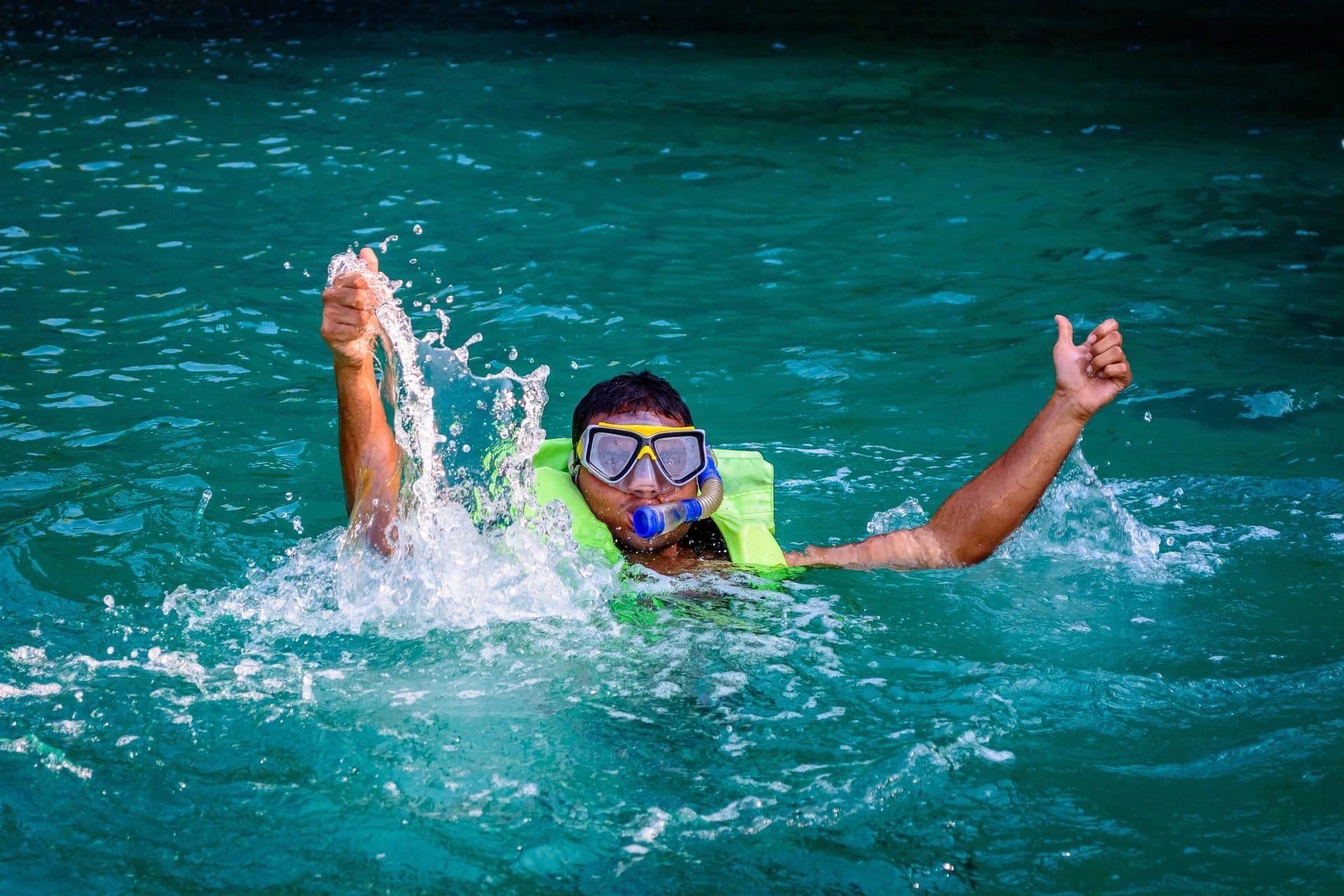 Una persona con máscara y chaleco saliendo a la superficie en agua turquesa con los dos brazos fuera del mar