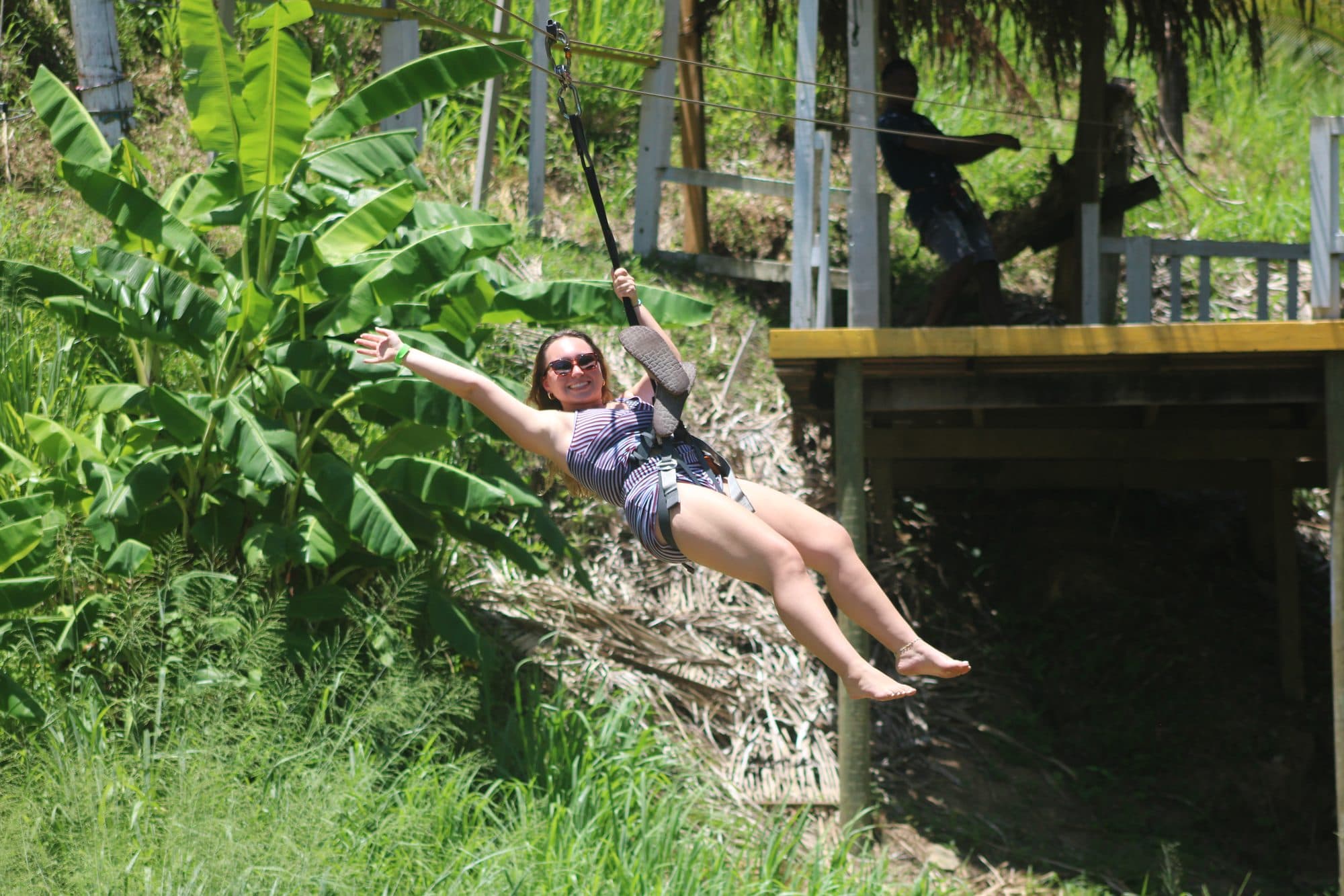 Una visitante bajando por la tirolesa sobre la selva verde con las piernas por delante, sonriendo